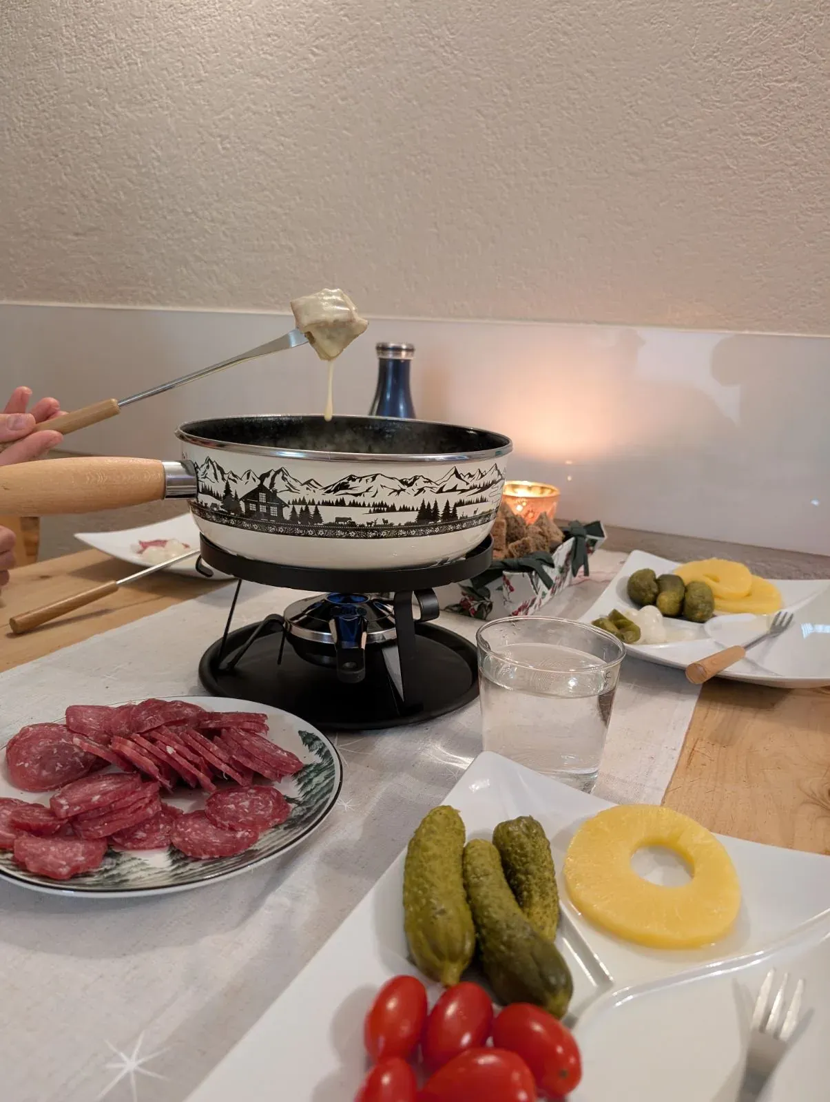 Käsefondue im Caquelon, dazu Salami, Gurken, Ananas und Tomaten