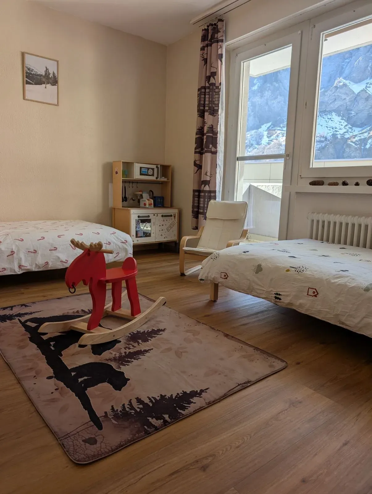 Zwei Betten, rotes Schaukelpferd und Spielküche, im Fenster eine Felswand