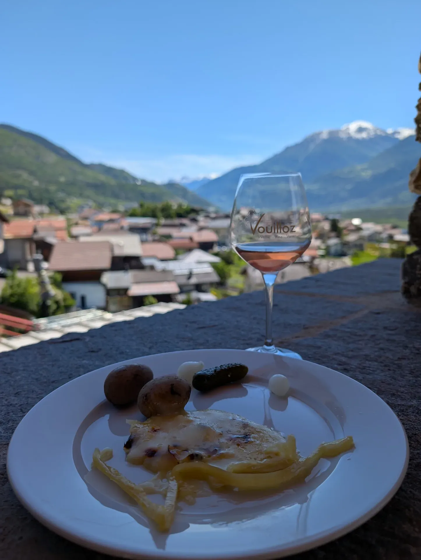 Raclette auf einem Teller und ein Glas Rosé, darauf steht Vouilloz