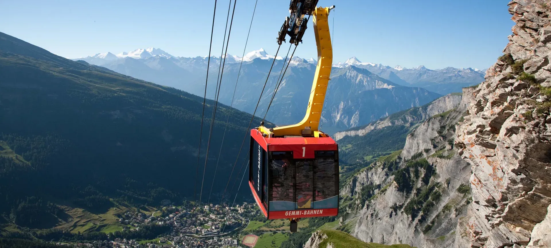 Rote Gondel der Gemmi-Bahnen an einer Felswand, darunter ein Tal