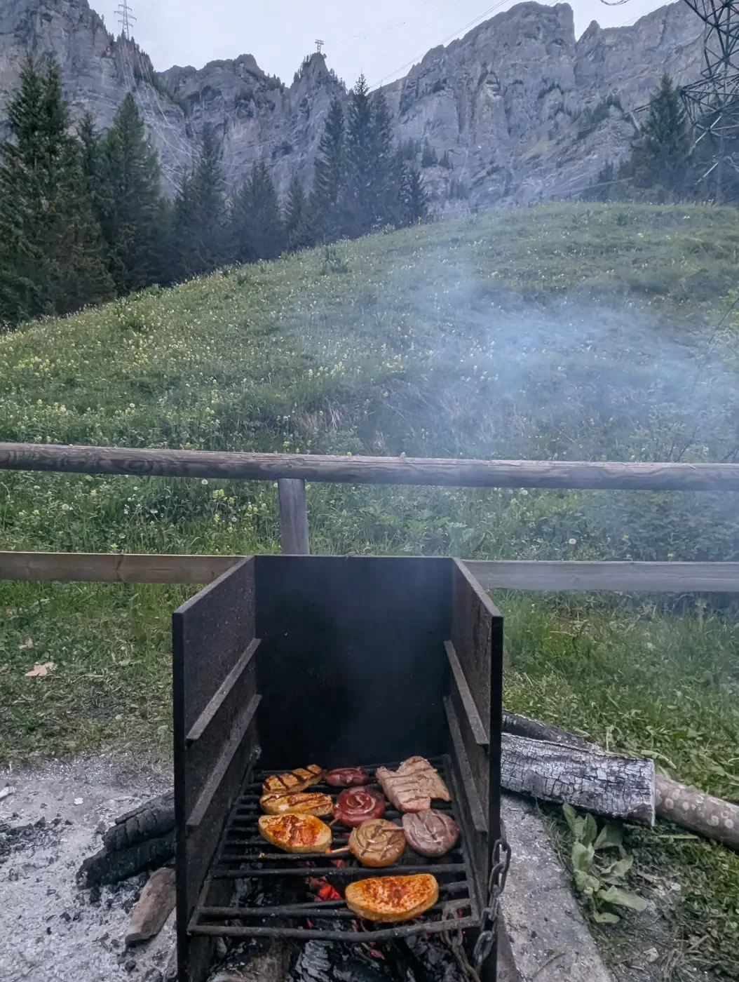 Grill mit Cervelat und Fleisch vor einer Alpweide und einer Felswand