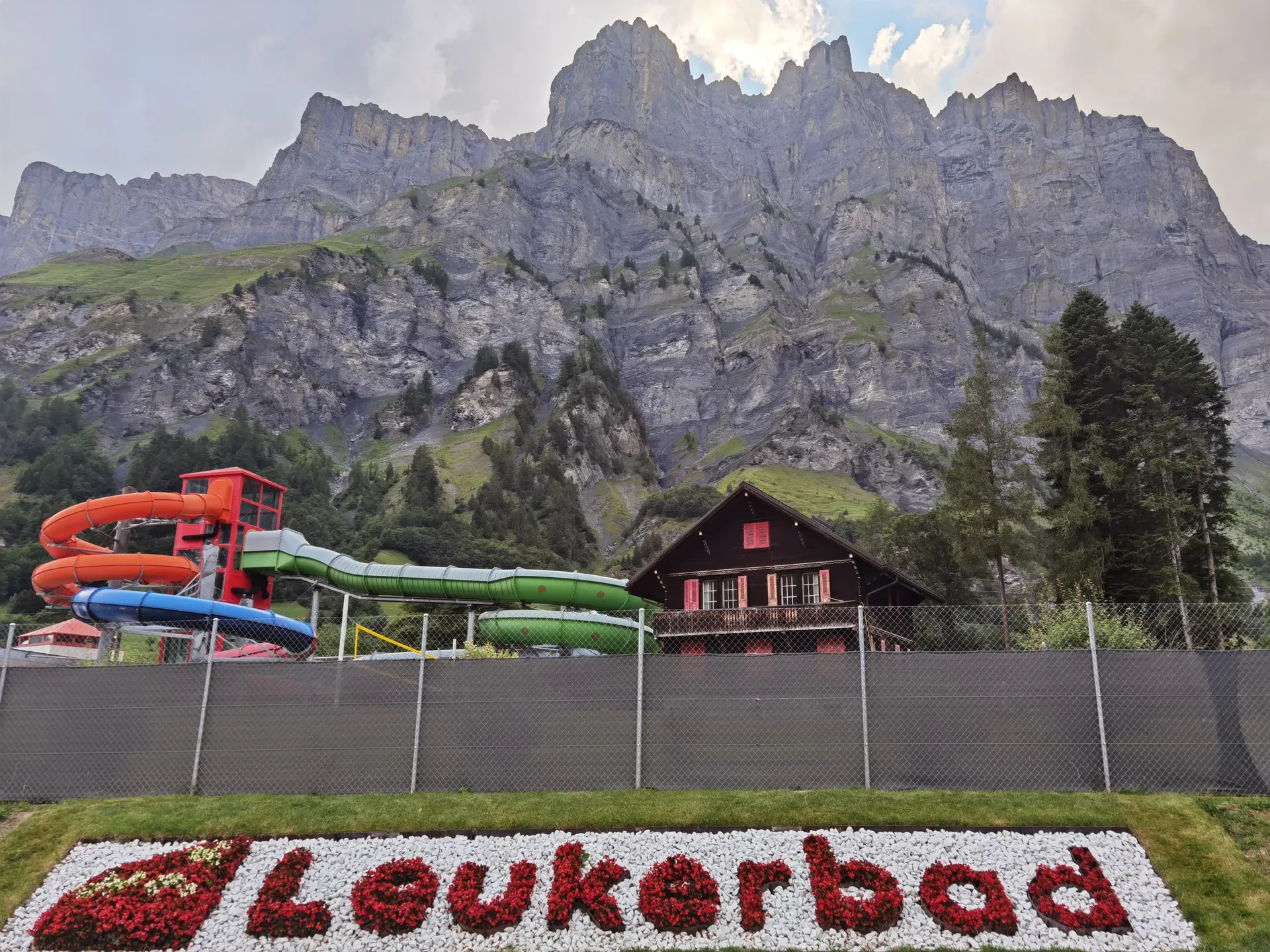 Blumen schreiben Leukerbad, dahinter bunte Rutschen, ein Holzhaus und eine Felswand