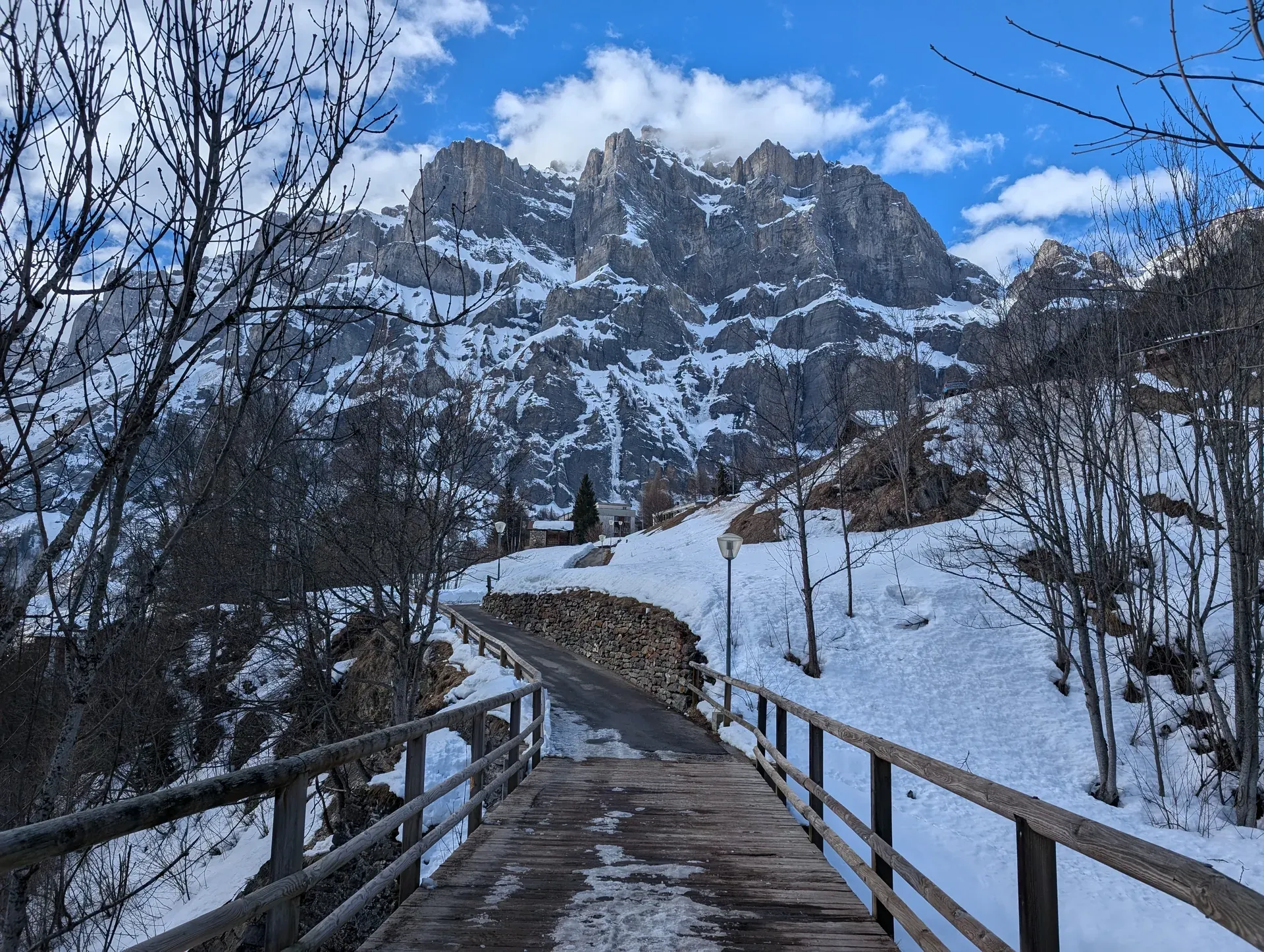 Holzbrücke und Geländer im Schnee, dahinter eine steile Felswand