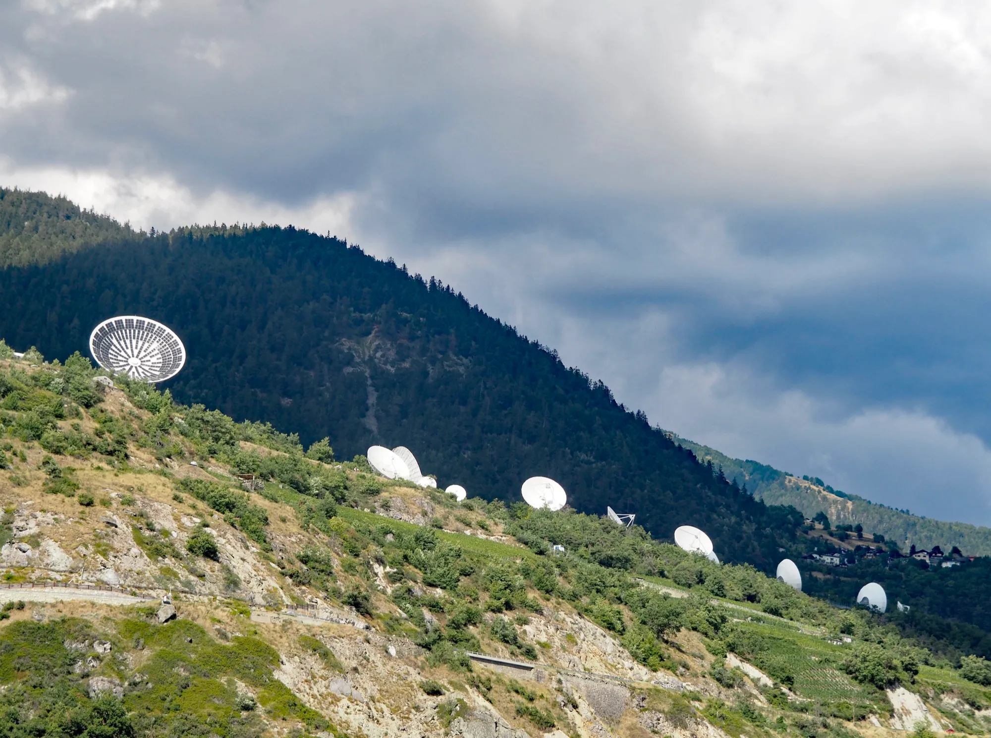 Weisse Satellitenschüsseln der Station Brentjong an einem bewaldeten Hang über dem Rhonetal