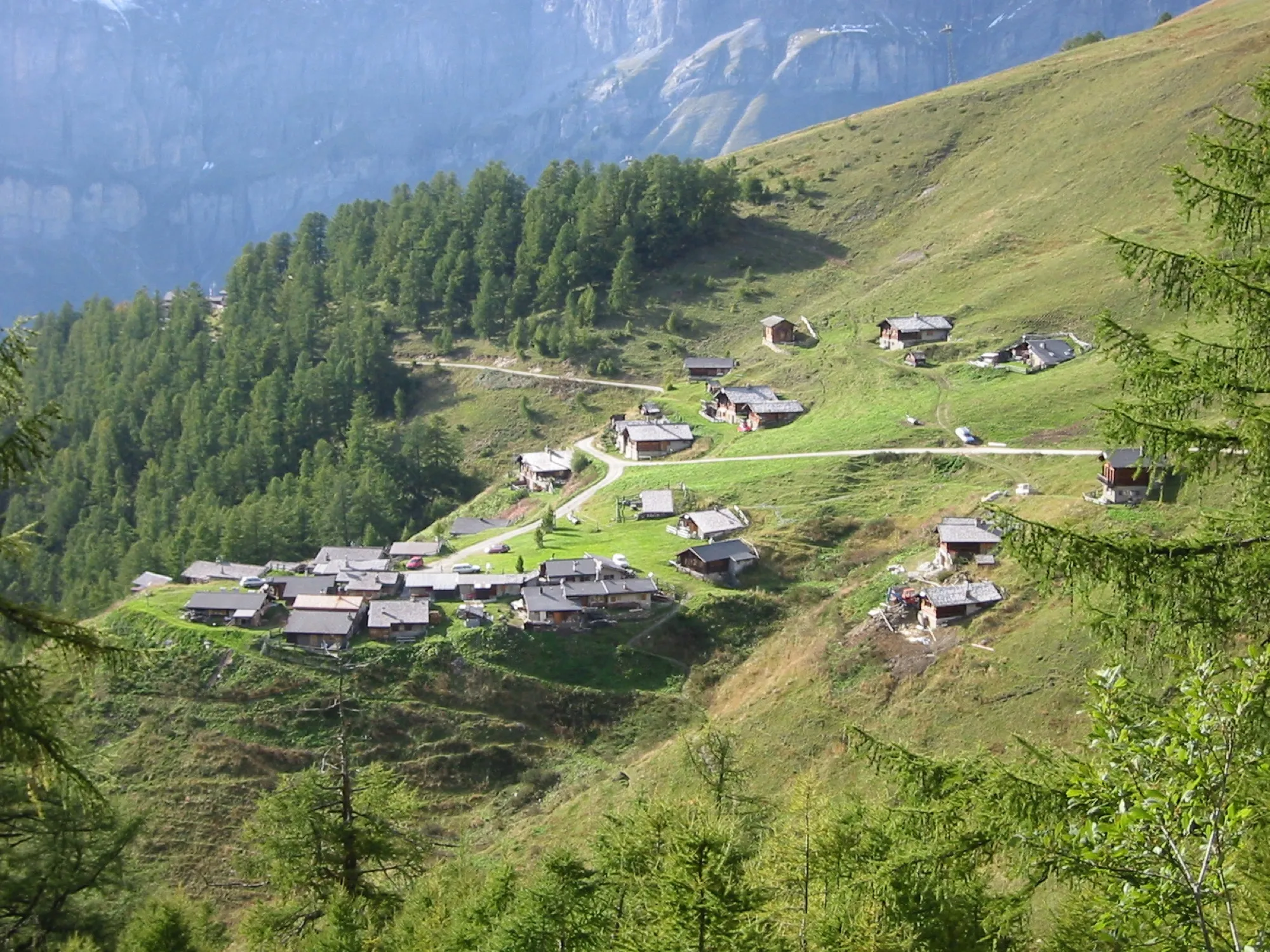 Alpweiler mit Holzhäusern an einem grünen Hang, dahinter die Felswände rund um Leukerbad