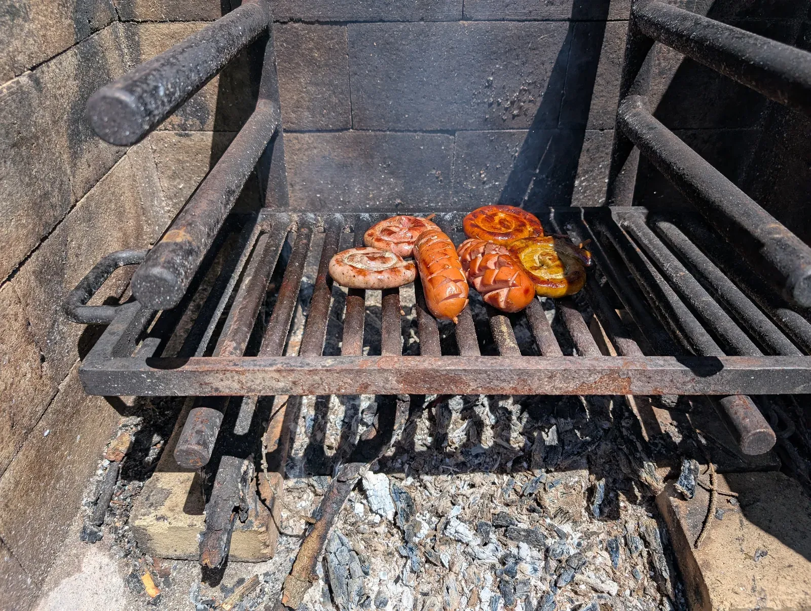 Bratwürste und eine Wurstschnecke auf einem schwarzen Grillrost über Glut