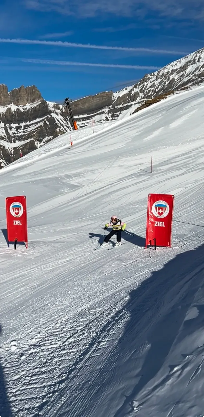 Kind mit Helm fährt Ski zwischen zwei roten Bannern mit der Aufschrift Ziel