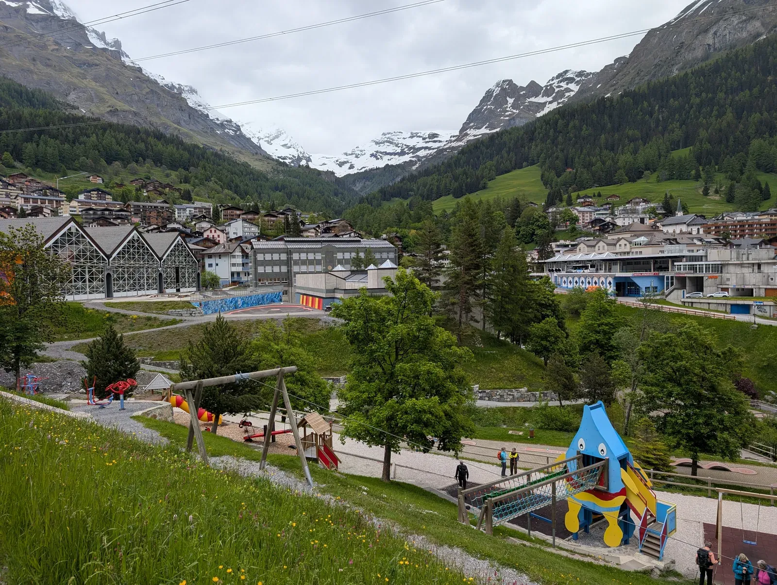 Spielplatz mit Rutsche und Schaukel auf einer Wiese, dahinter ein Bergdorf
