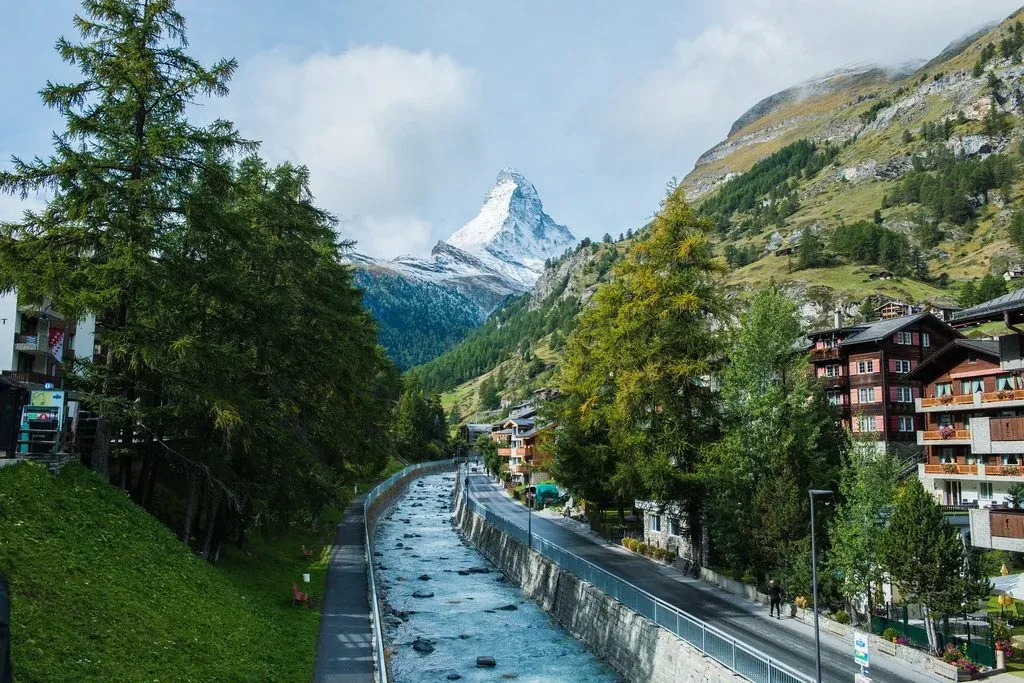 Bach und Weg durch ein Dorf, hinten das Matterhorn zwischen Bäumen