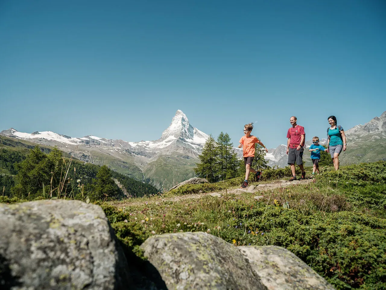 Familie mit zwei Kindern auf einem Wiesenweg, dahinter das Matterhorn