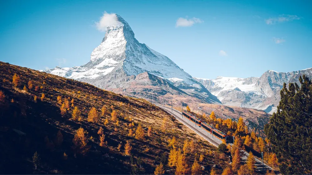 Rote Bahn zwischen herbstlichen Lärchen, dahinter das Matterhorn