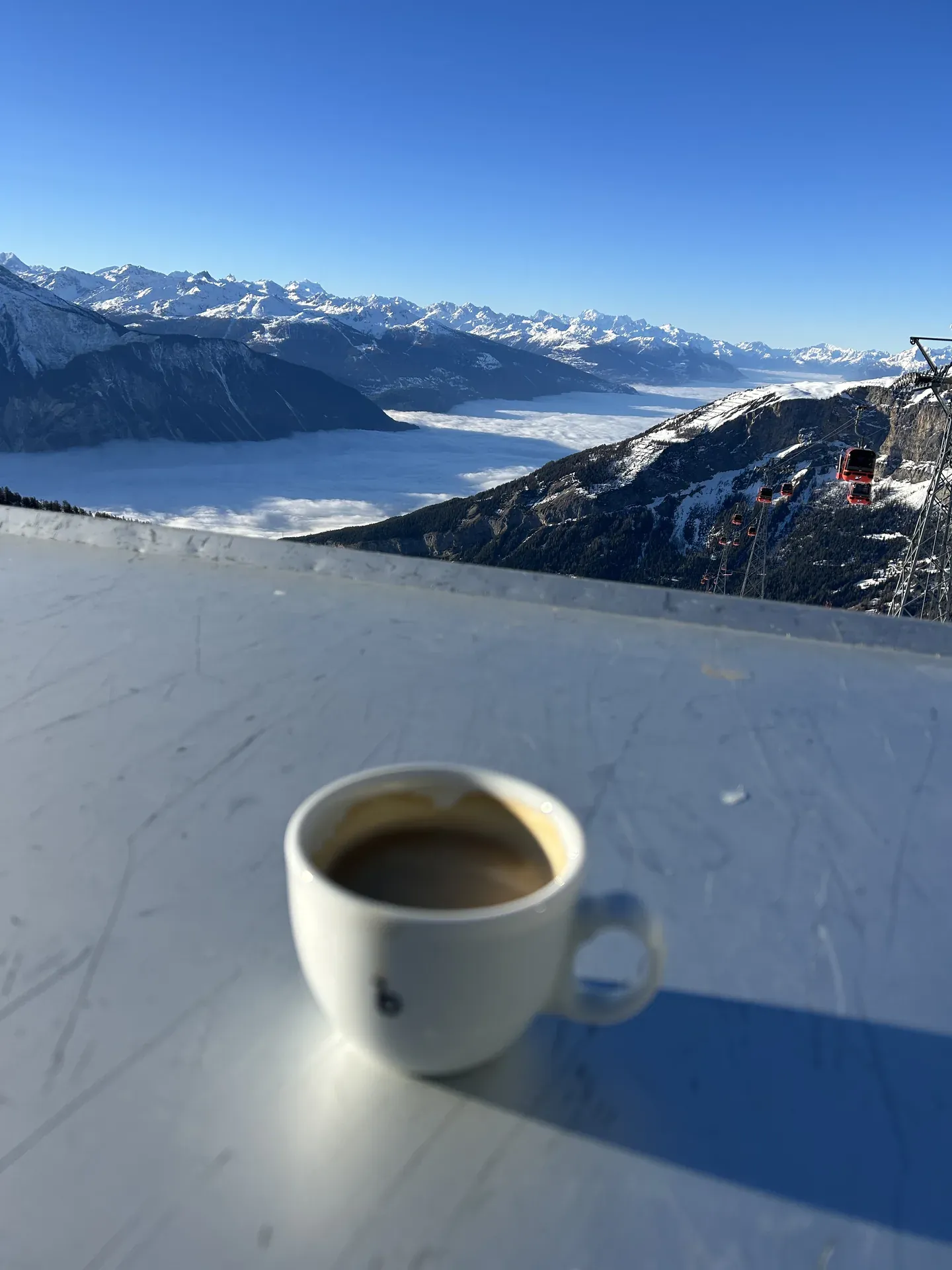 Kaffeetasse auf einem Tisch, rote Gondeln über einem Tal im Hochnebel