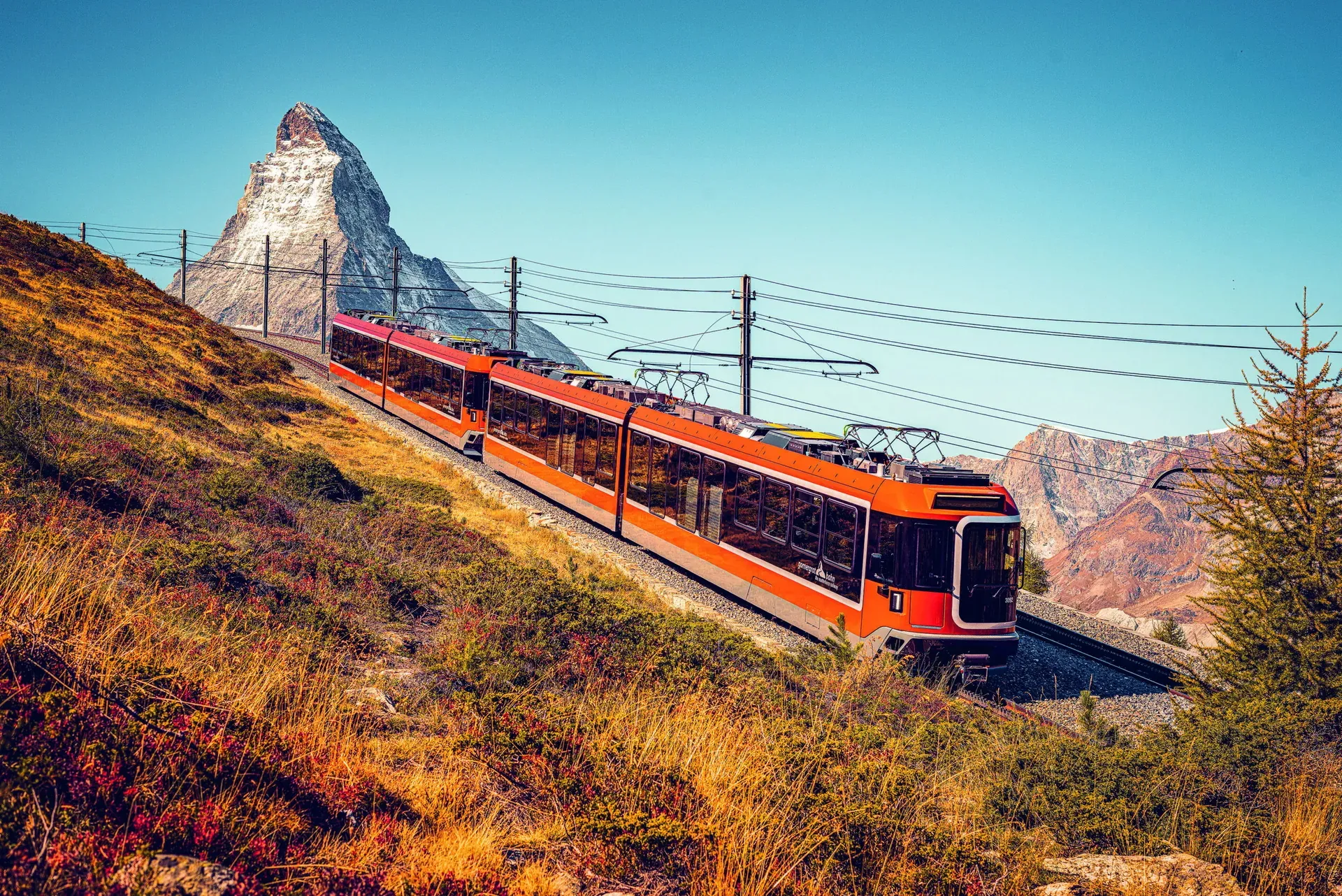 Orange Bahn auf einem Hang, dahinter das Matterhorn und Leitungen